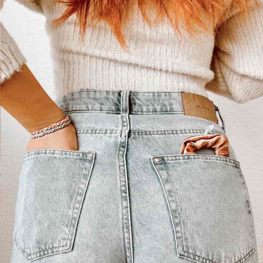 Woman wearing light denim jeans with a hairband in her back pocket and a knitted sweater.