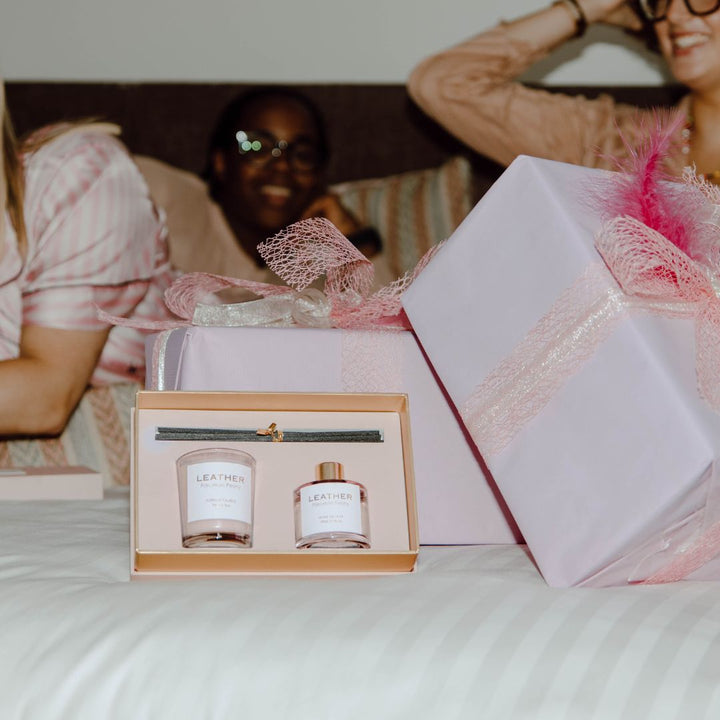 Pink Leather Porcelain Peony Gift Pack with diffuser and candle on a bed, surrounded by elegant gift boxes.