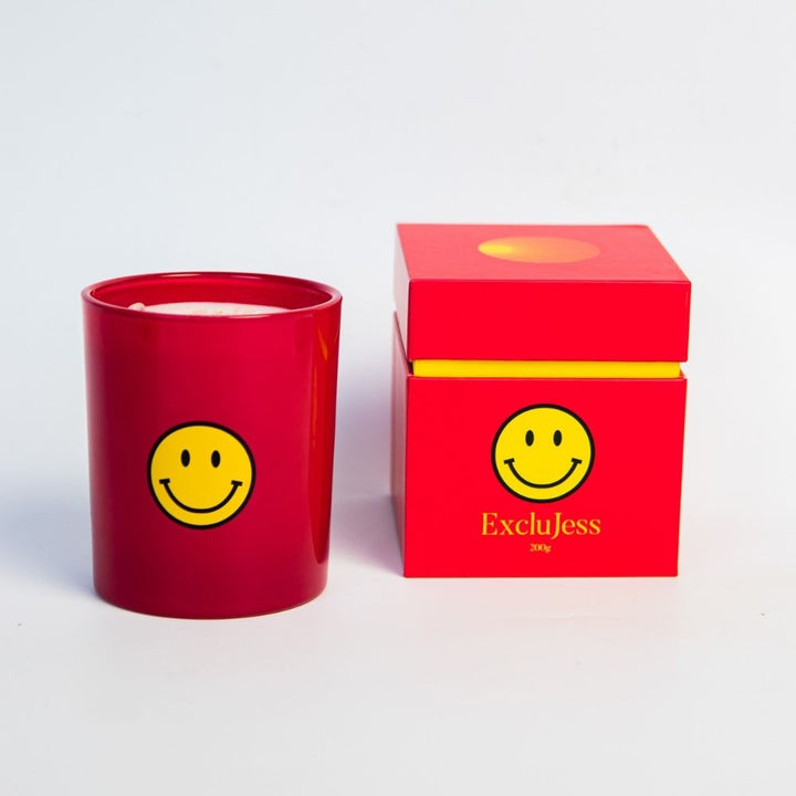 Smiley Kaars in rode houder met gele smiley en kleurrijke verpakking voor positieve vibes.