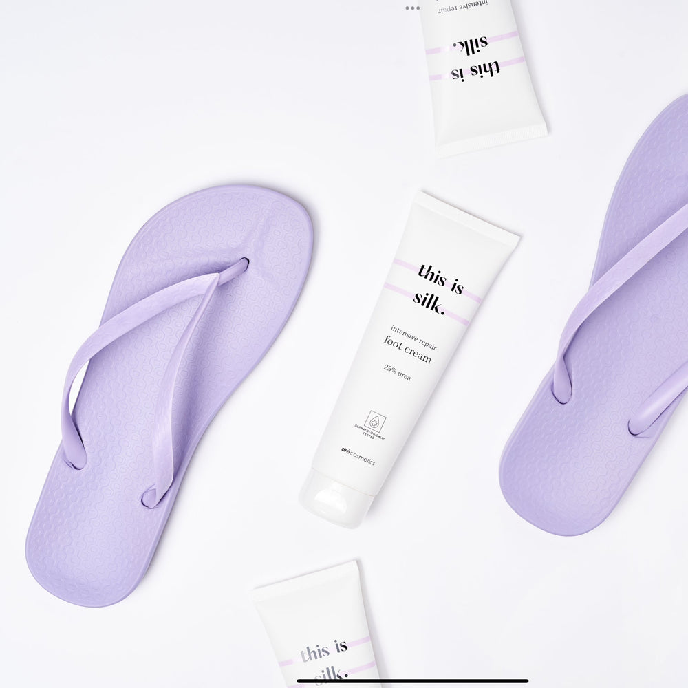 Voetcrème 'this is silk' met 25% urea, omringd door paarse slippers op een witte achtergrond.