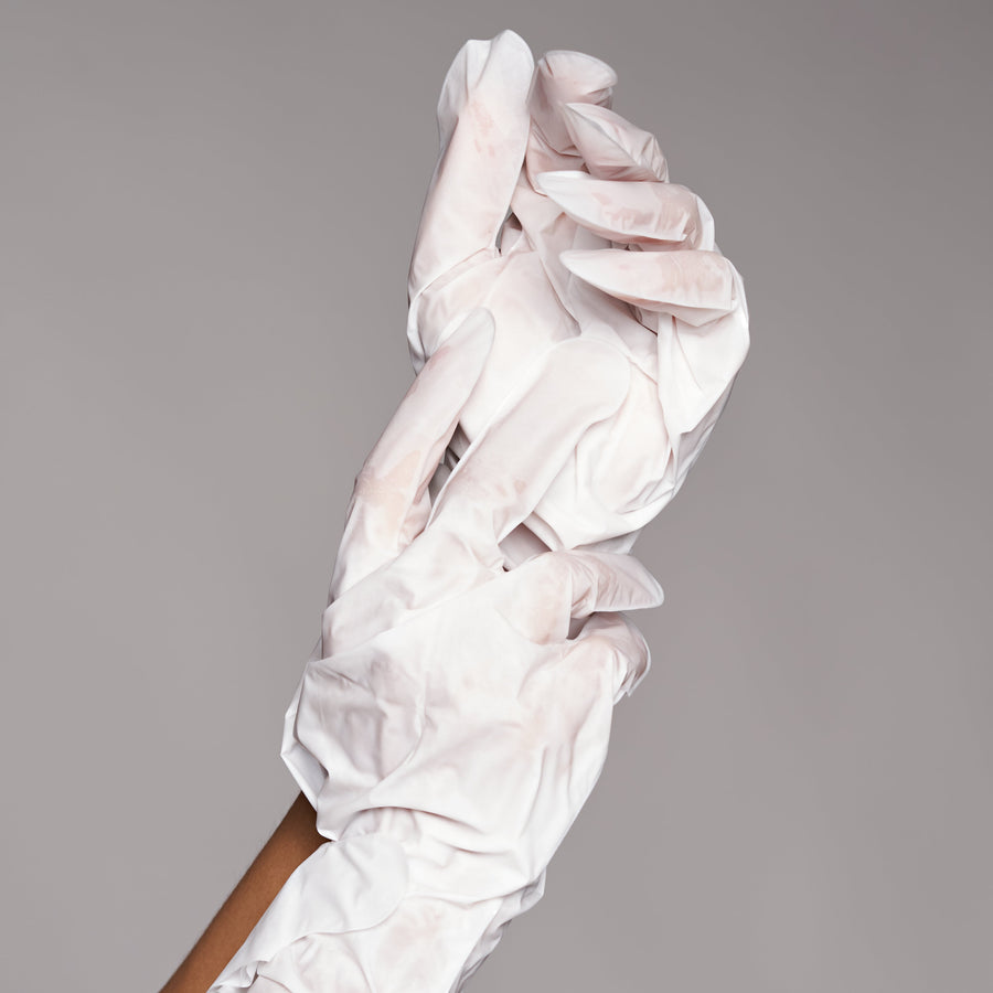 Hands wearing white treatment gloves for intensive moisturizing foot or hand mask application.
